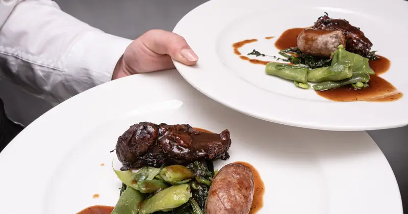 Stock photograph of a chef carrying two plated meat dishes.